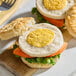 A sandwich with a Yo Egg Plant-Based Egg Patty and vegetables on a cutting board.