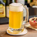 A glass mug of yellow liquid on a coaster.