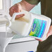 A person pouring a jug of Softsoap liquid hand soap into a sink.