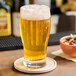 A glass of beer with bubbles on a coaster on a wooden bar.