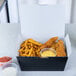 A black folded paper take-out box with chicken and fries inside.