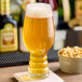 A glass of Hopzoil MAJIK® Chinook Hop Extract in a glass of beer on a table with a bowl of nuts.