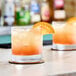 A close up of two glasses of Les Vergers Boiron Sudachi 100% Fruit Puree with orange slices on top.