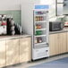 A white glass door merchandiser refrigerator displaying various beverages in a break room setting.