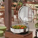 An Acopa stainless steel chafer with a glass lid on a table with food inside.