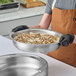 A round stainless steel food pan filled with rice and chicken, being held by a person wearing black gloves and a brown apron.
