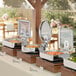 An outdoor buffet table with an Acopa Manchester stainless steel chafer on it filled with food.