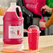 A gallon jug of Hometown Provisions Fruit Punch Slushy 5:1 Concentrate next to a cup of prepared fruit punch slushy.