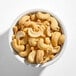 A white bowl filled with large whole roasted unsalted cashews.