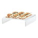 A Cal-Mil clear acrylic U-shape display riser with figs and cheese on it.