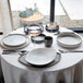 A white round stoneware soup or cereal bowl with angled edges, set on a dining table with other tableware.