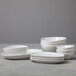 A set of matte white oval bowls and plates, including sauce or tasting bowls, arranged in stacks on a gray surface.