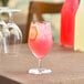 A glass of pink drink with a slice of lemon on a table.