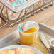 A tray with a plastic cup of SunCup orange juice with a plastic lid on top and a knife on a napkin.