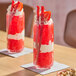 A tall glass of bright red strawberry slushy with a layer of cream, topped with whipped cream, a strawberry slice, and TWIZZLERS candy sticks.