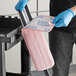 A person in blue gloves using a pink Lavex dry mop pad to clean a kitchen counter.
