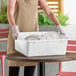 A white polypropylene bus tub or food storage box being used to collect dishes from a table.