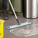 A person mopping the floor with a Lavex blue microfiber mop pad attached to a mop handle.