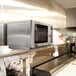 An Amana medium duty stainless steel commercial microwave on a counter in a kitchen.