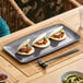 A dark gray rectangular melamine platter holding three bao buns, displayed on a dining table.
