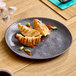 A dark gray round melamine plate with a speckled pattern, shown holding three dumplings with sauce and green onions.