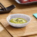 A small light gray round melamine ramekin filled with green paste and garnished with seeds.