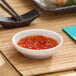 A small white round melamine ramekin filled with a red dipping sauce.