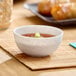 A small white round melamine ramekin filled with sauce and garnished with green onions.