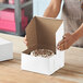 A white bakery box with an open lid containing a cake inside.