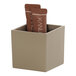 A taupe square resin crock holding small brown packets.