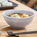 A light gray round melamine bowl filled with soup and dumplings.