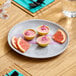 A light gray melamine plate featuring three grapefruit mousse cups and three grapefruit slices.