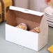 A close up of a white Baker's Lane cake box full of pastries with frosting.