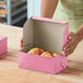 A pink bakery box containing pastries on a wooden surface.