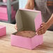 A pink bakery box containing a chocolate cake with pre-sliced portions.