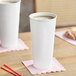 A white 24 oz. double wall insulated paper hot cup filled with a beverage, placed on a pink napkin.