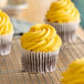 A chocolate cupcake with bright yellow frosting, displayed on a cooling rack.