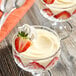 A glass dessert dish filled with white chocolate pudding, garnished with sliced strawberries and a swirl of whipped cream.