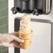 A hand holding a soft serve ice cream cone filled with Flora Professional Dairy-Free Vegan Soft Serve Ice Cream.