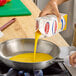 A carton of Papetti's liquid egg yolk being poured into a stainless steel frying pan on a stove.
