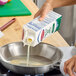 A carton of Abbotsford Farms cage-free liquid egg whites being poured into a stainless steel frying pan.