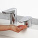 A person using a Bobrick polished chrome deck-mount automatic liquid soap dispenser to wash their hands at a sink.