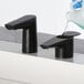 A close-up of a Bobrick matte black deck-mount automatic foam soap dispenser.