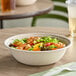 A compostable wide fiber take-out bowl filled with salad and shrimp.