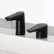 Two Bobrick matte black deck-mount bathroom faucets on a white counter.