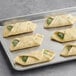A baking tray with several unbaked spinach and ricotta croissants.