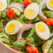 A salad featuring sliced hard cooked eggs, spinach leaves, grape tomatoes, red onion, and bacon bits.