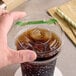 A clear compostable plastic cold cup lid with a straw slot being placed on a cup of iced beverage.