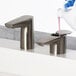 A hand in a glove pouring liquid into a Bobrick brushed nickel deck-mount soap dispenser over a sink.