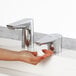 A close-up of a hand using a Bobrick polished chrome deck-mount automatic foam soap dispenser.
